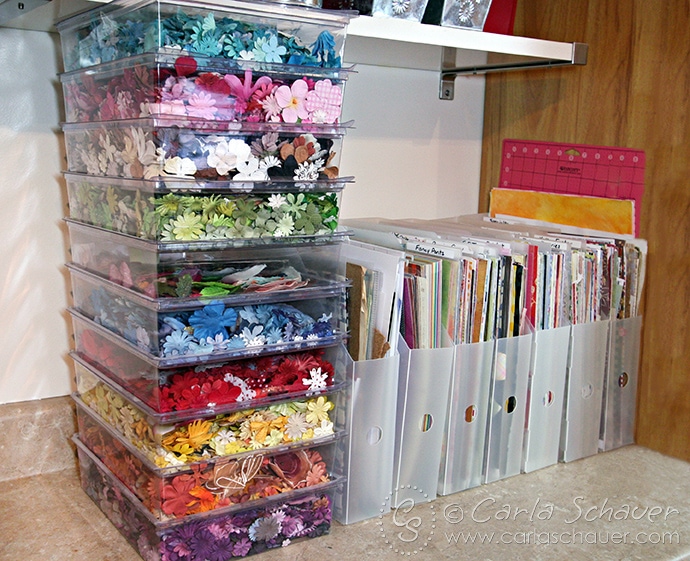 plastic containers filled with scrapbook paper and paper flowers on counter.