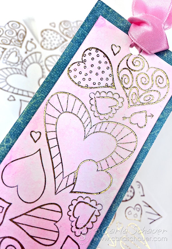 Pink watercolored bookmark with gold foil hearts and blue border on white background. 