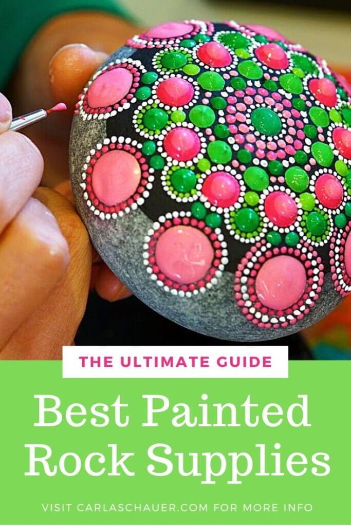 Hands painting pink and green dots to make a mandala design on a gray rock.