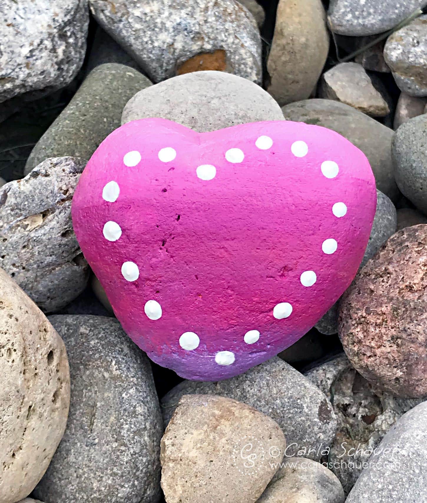 Heart shaped rock painted with a pink and purple ombre gradient, with white dots around border.