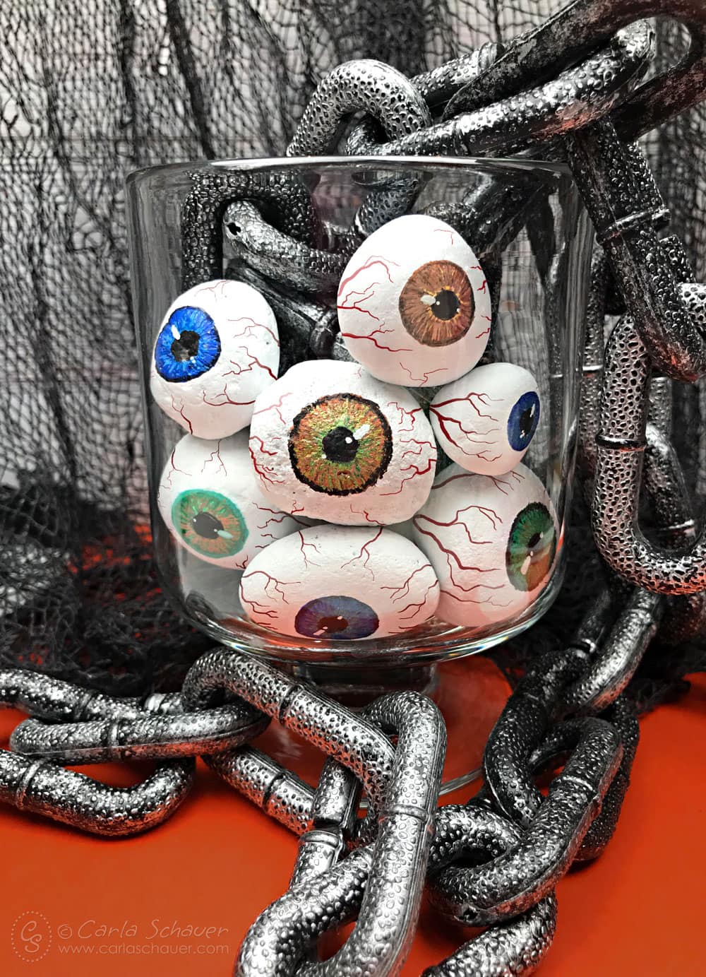 Painted rock eyeballs in jar with chain and black mesh background.