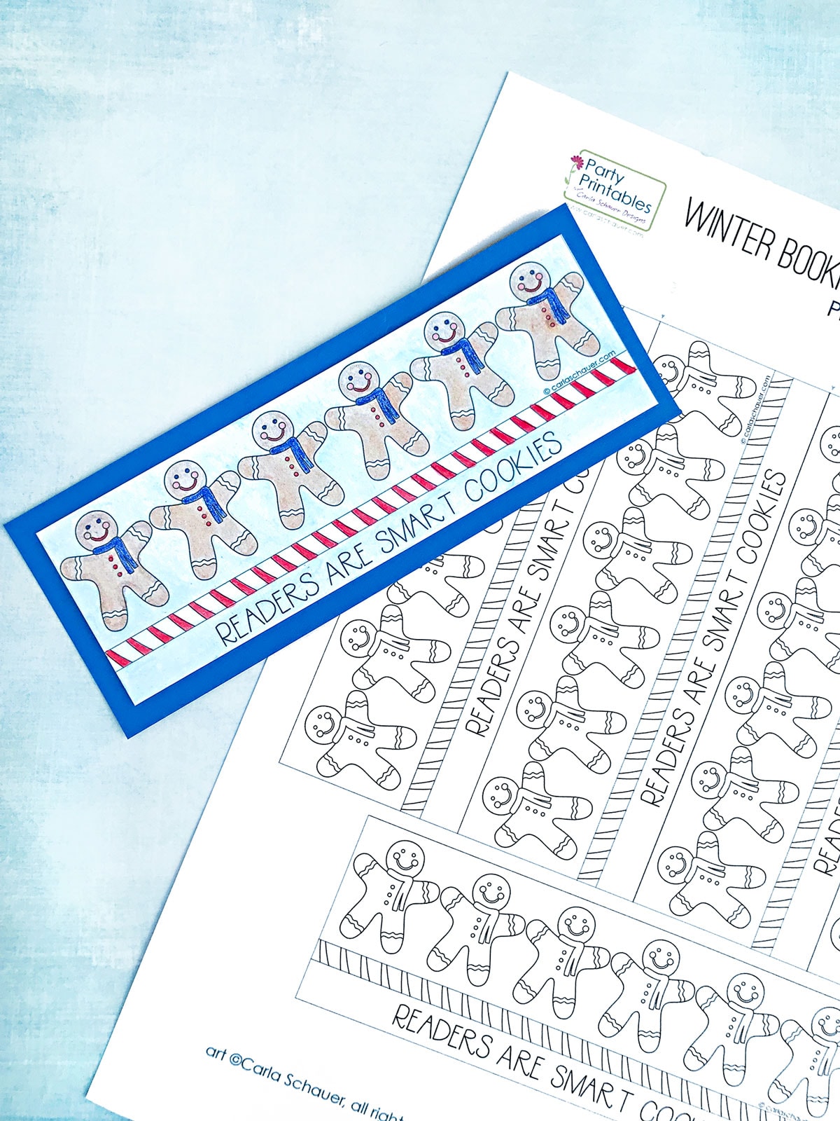 Colored in gingerbread man bookmark layered on printed bookmark sheet and blue background.