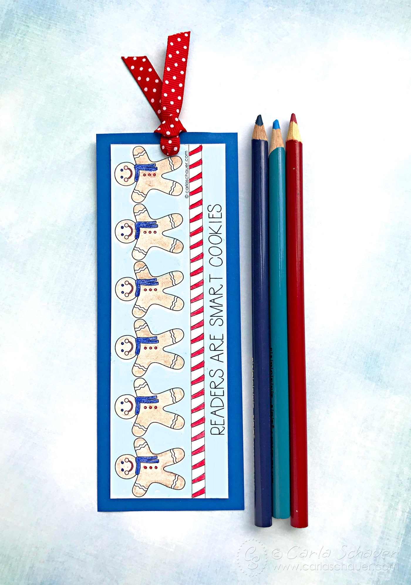 Printable winter bookmark after coloring, next to colored pencils on blue background.
