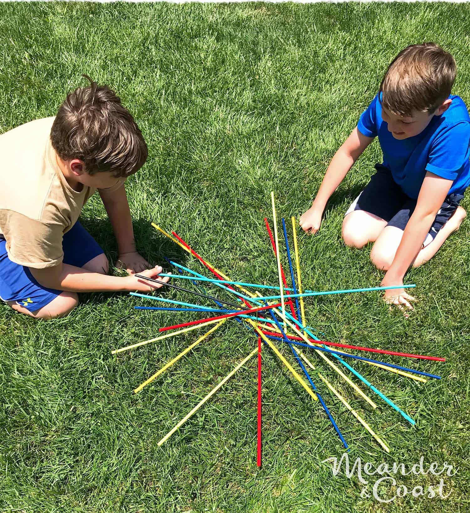 two children in grass, playing with giant pick up sticks game