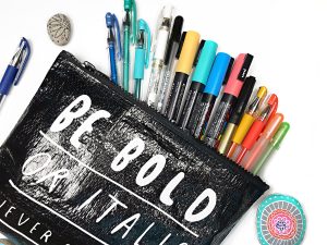 Black pouch of paint markers and gel pens, with painted rocks on white background.