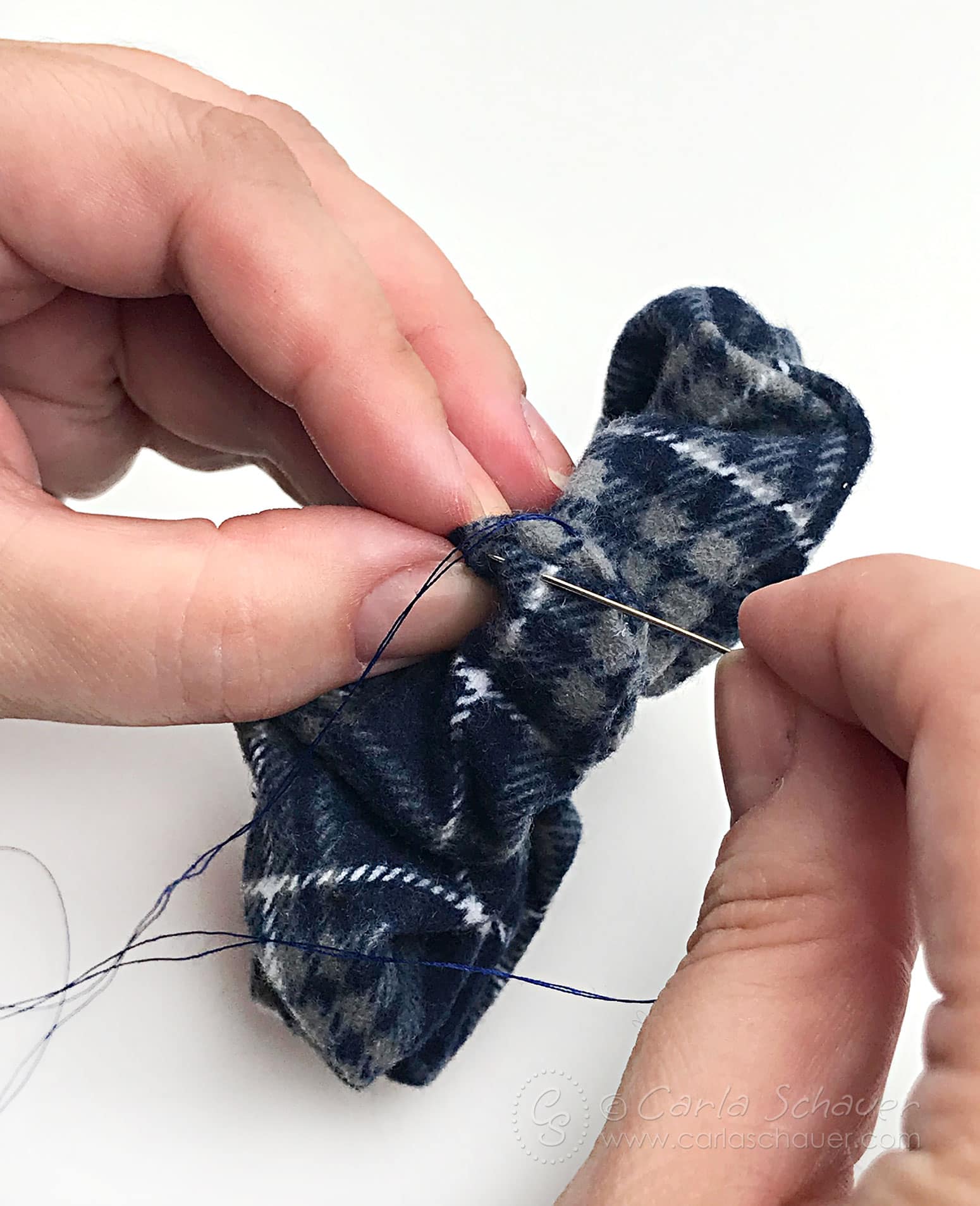 Hands sewing a plaid scrunchie closed.
