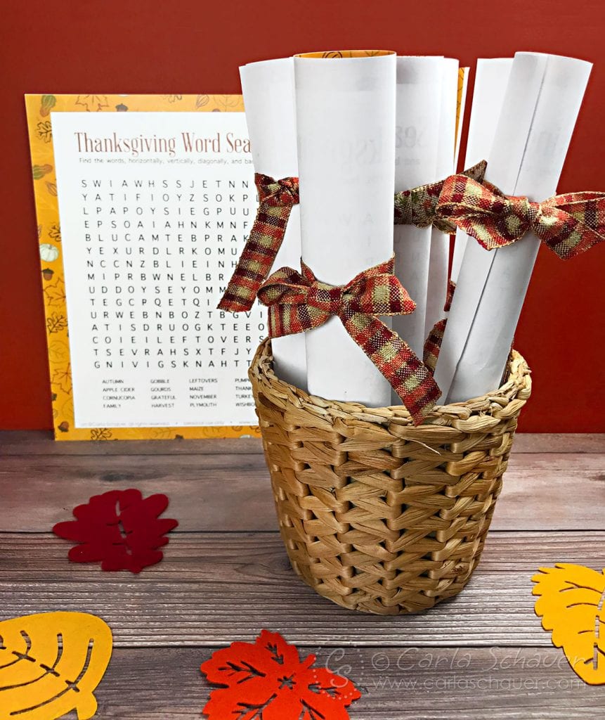 Rolled word search printables tied with fall ribbon, in basket, on wood table.
