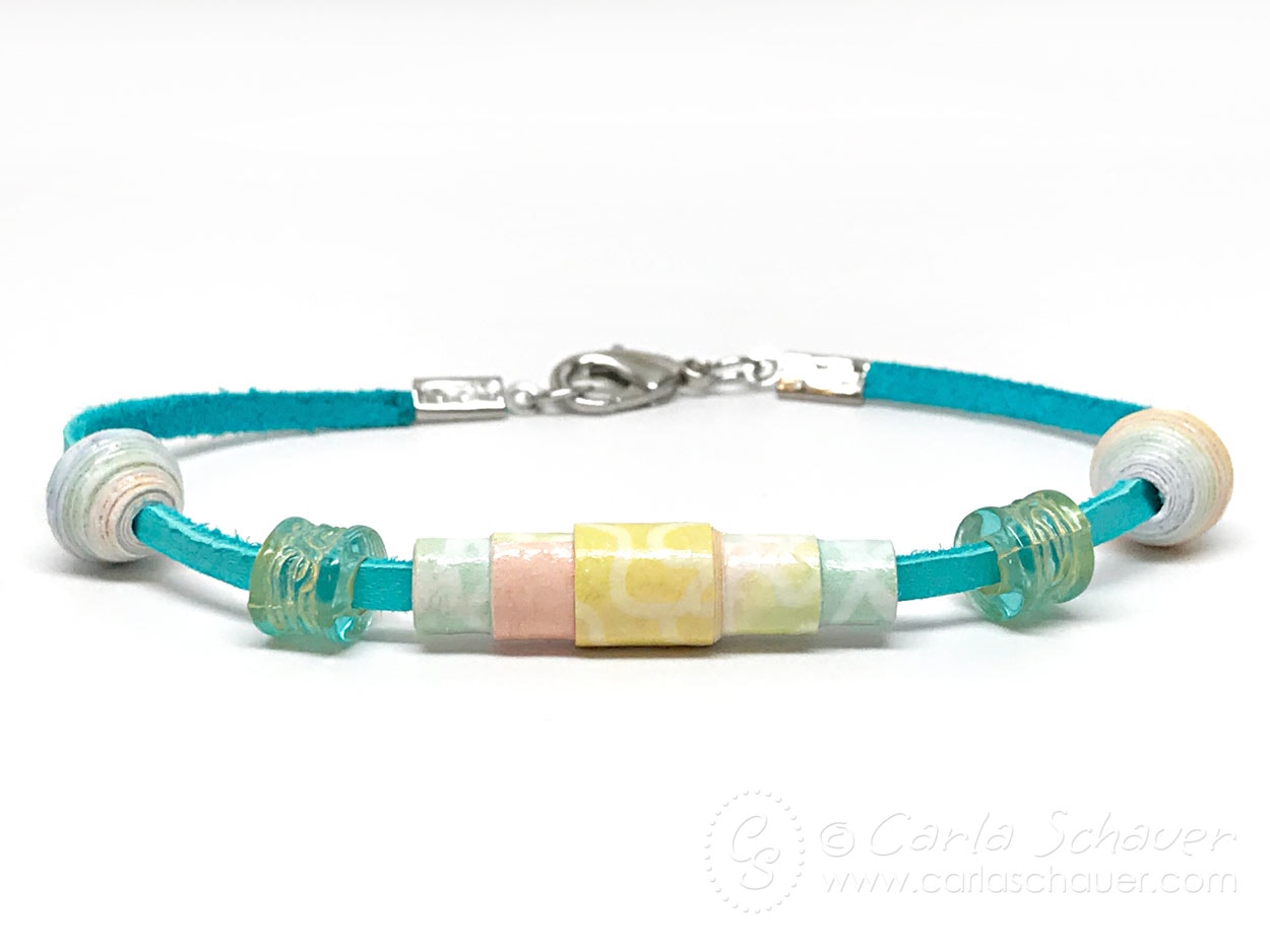 Rainbow Bracelet made with paper beads strung on teal leather cord, sitting on white background.