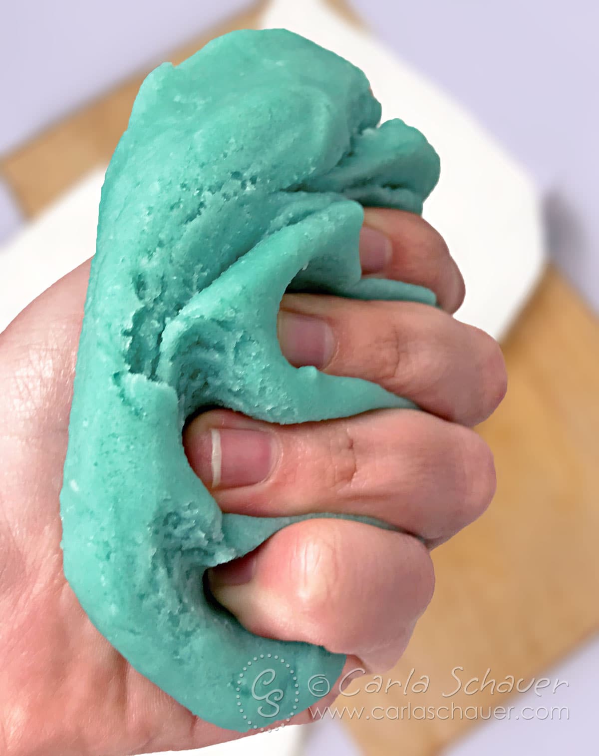 Hand squishing teal homemade cooked playdough.
