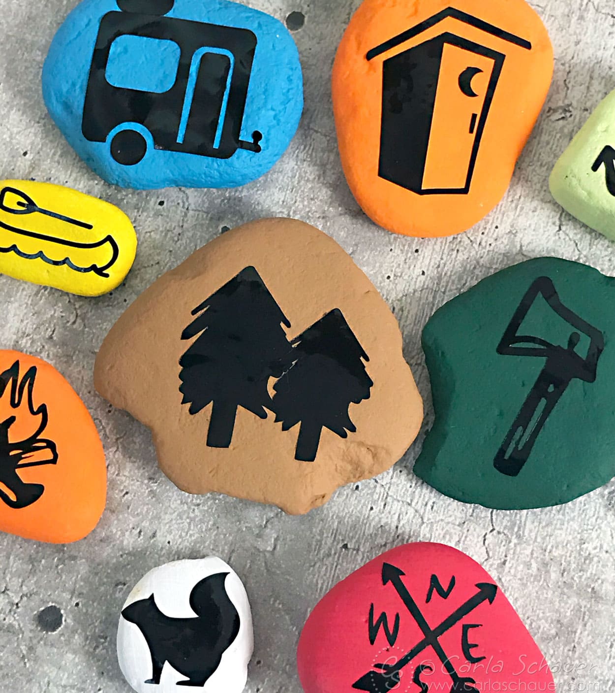 Closeup photo of painted rock stones with black camping icons.