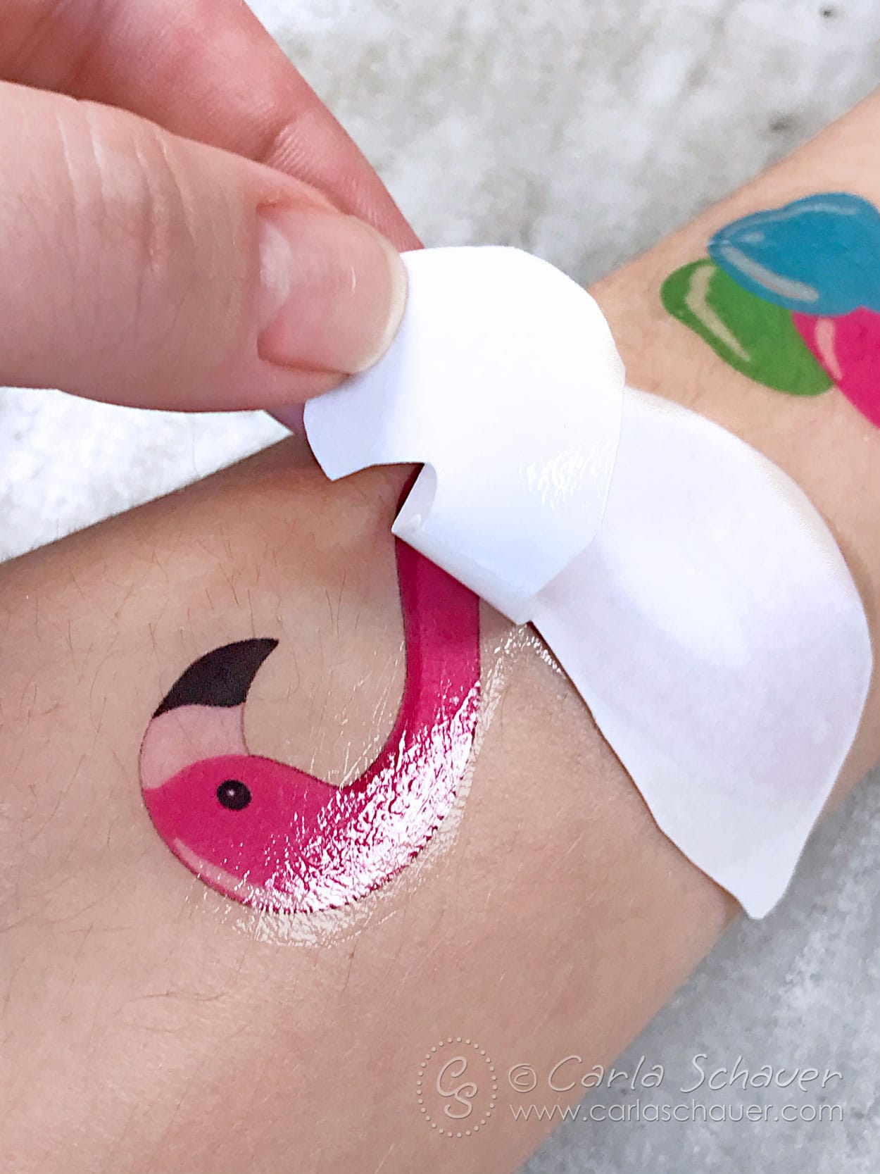Peeling white paper from flamingo summer temporary tattoo on skin.