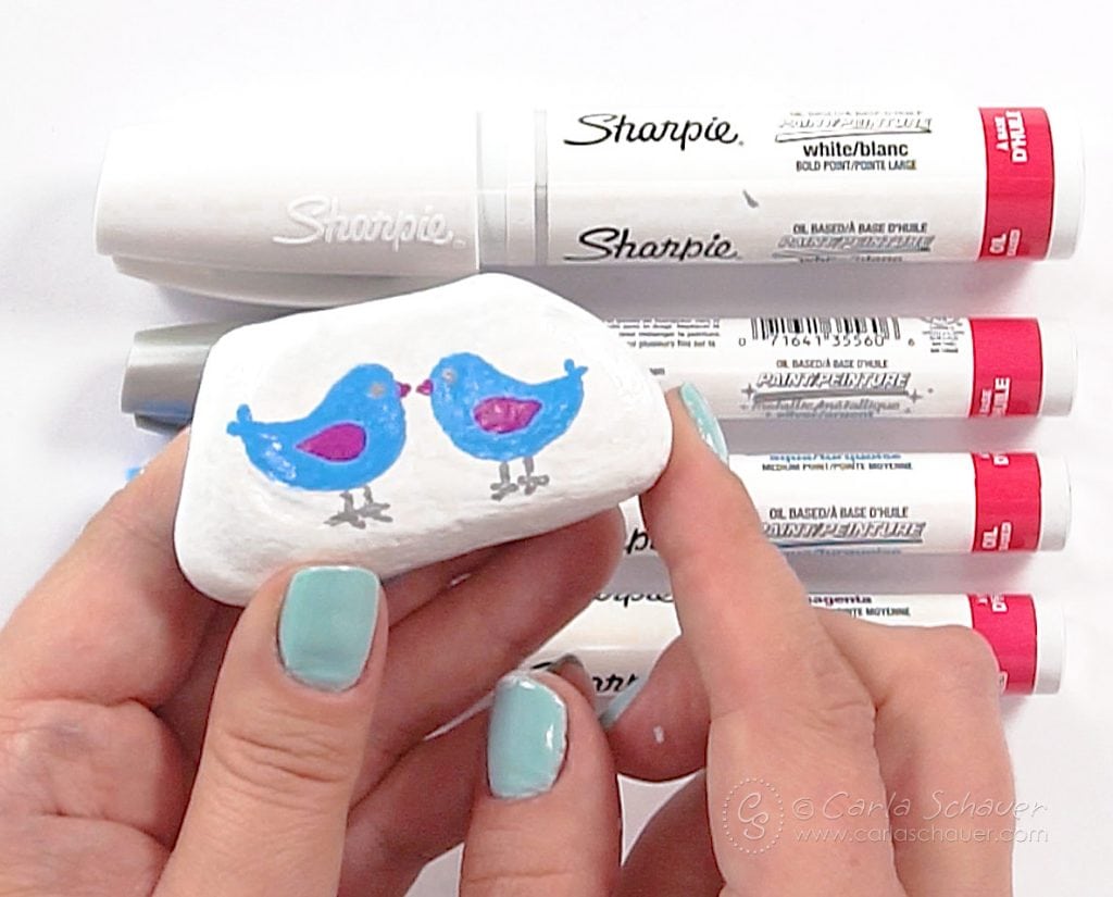 White rock with blue and pink painted birds, with markers in background.
