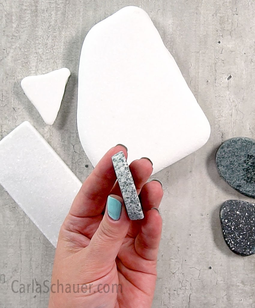 Hand holding a slice of river rock used for making painted rock art. More white and speckled rock slices in background.