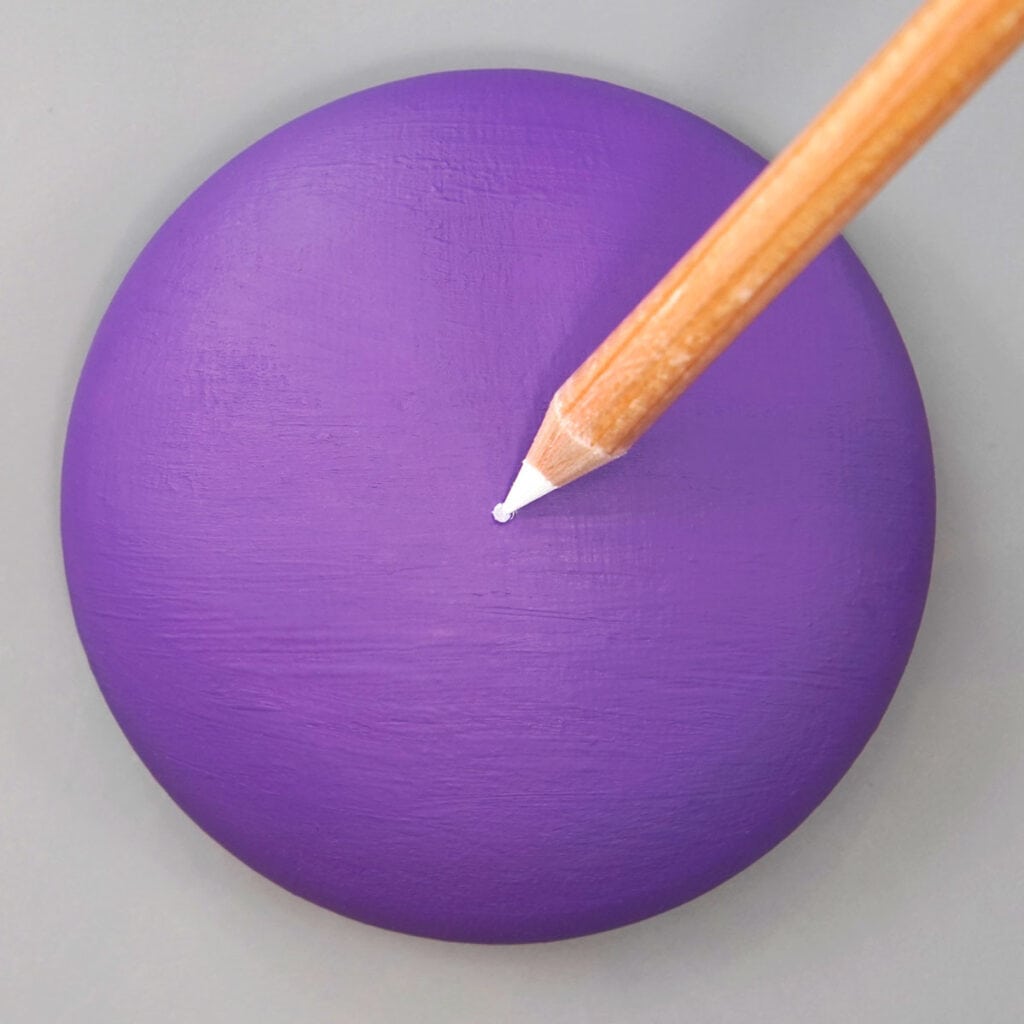Round purple rock on gray background. wood pencil with white lead is making a dot in the center of the rock.