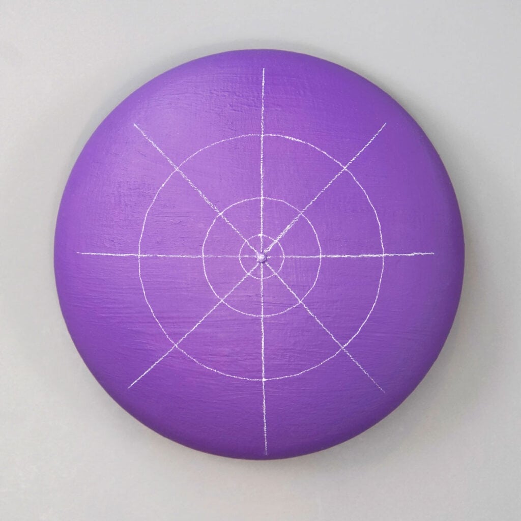 purple painted circle rock with white grid lines. Straight lines divide rock into 8 sections. 3 concentric circle lines.