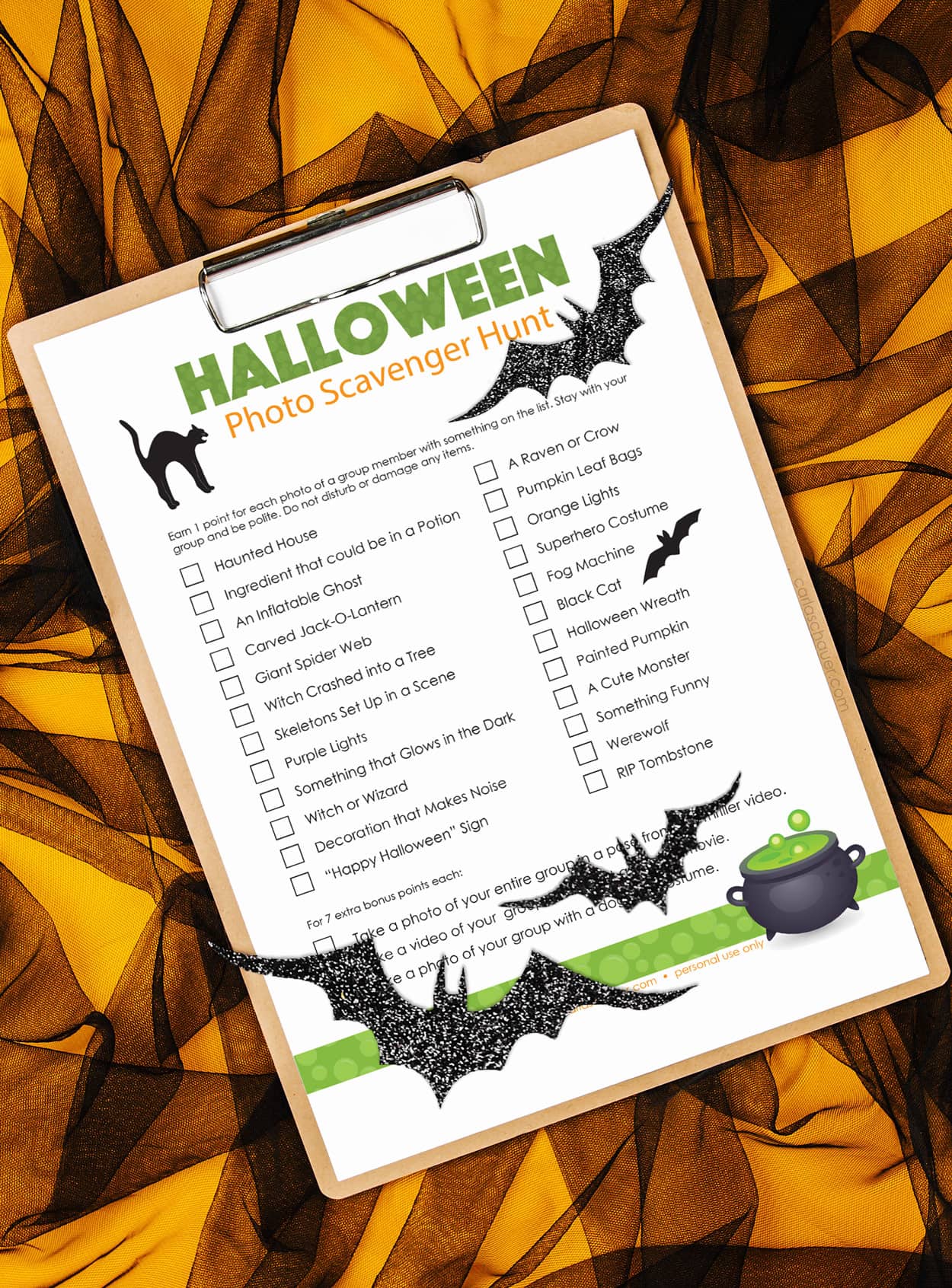 Orange background covered by black mesh, with clipboard. Attached to clipboard is a printed Halloween Scavenger Hunt list with 3 glittery black bats sitting on top.