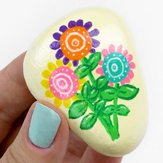 cream colored stone painted with 3 flowers in pink, green, purple, orange, and blue