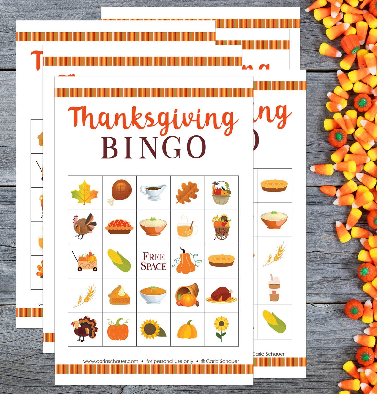 Six printed Thanksgiving Bingo Game Boards on a gray wood background, next to a cluster of candy corn and pumpkins. Each bingo card is filled with colorful fall icons and text reading "Thanksgiving BINGO" across the top.