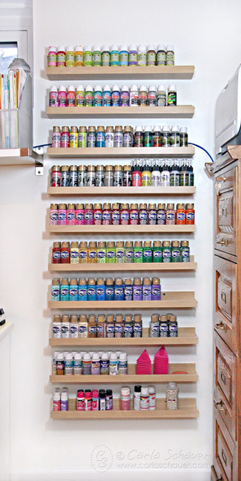 vertical wood shelves filled with colorful acrylic paint in rainbow order