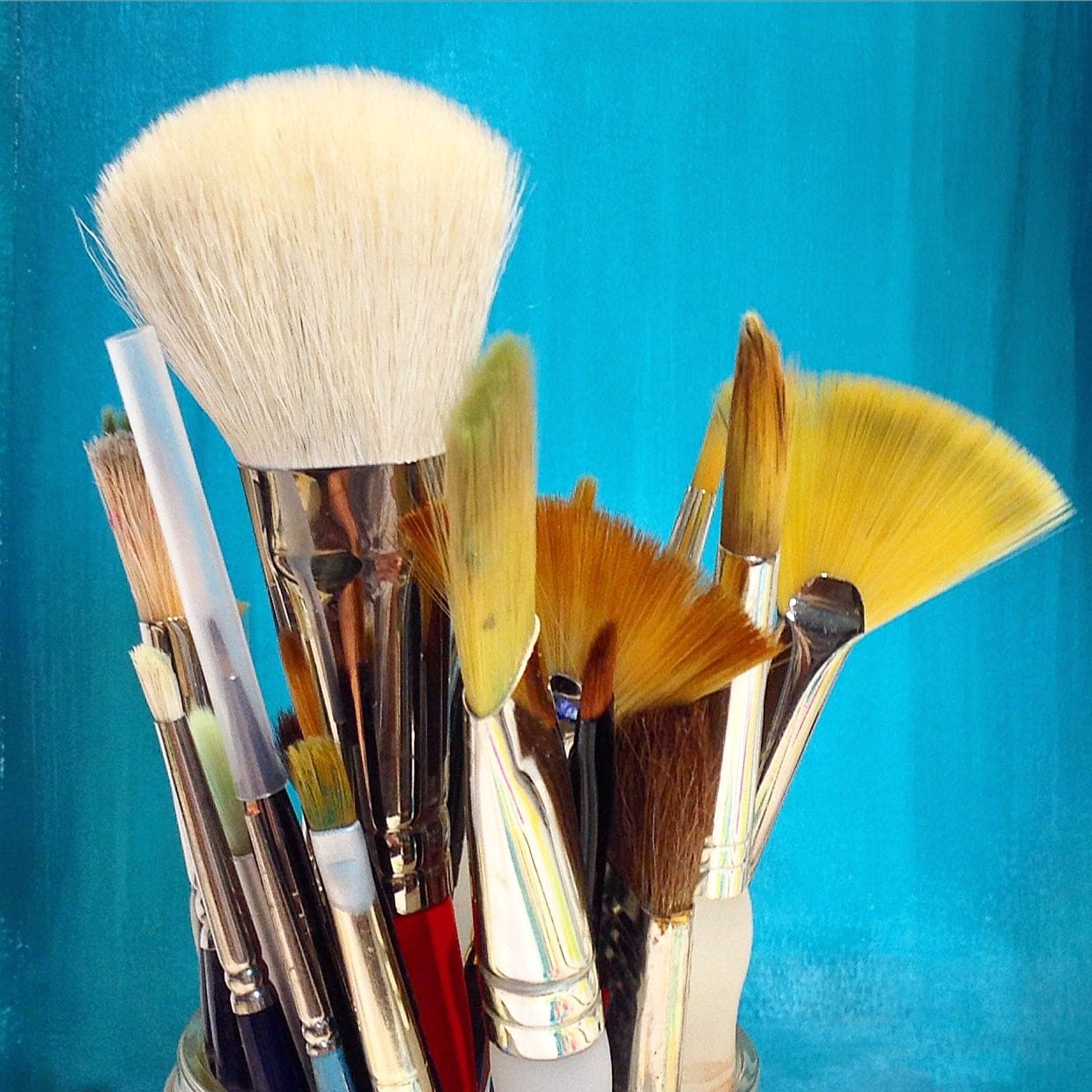 jar of assorted art paint brushes, in front of a blue painted background