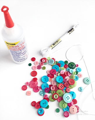 red, green, blue, and pink buttons in a pile next to white embroidery floss and a bottle of glue