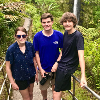 3 teenagers on a walkway in front of lush green vegetation