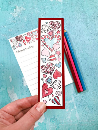 heart bookmark colored in red, pink and blue, held in front of matching reading log and blue background