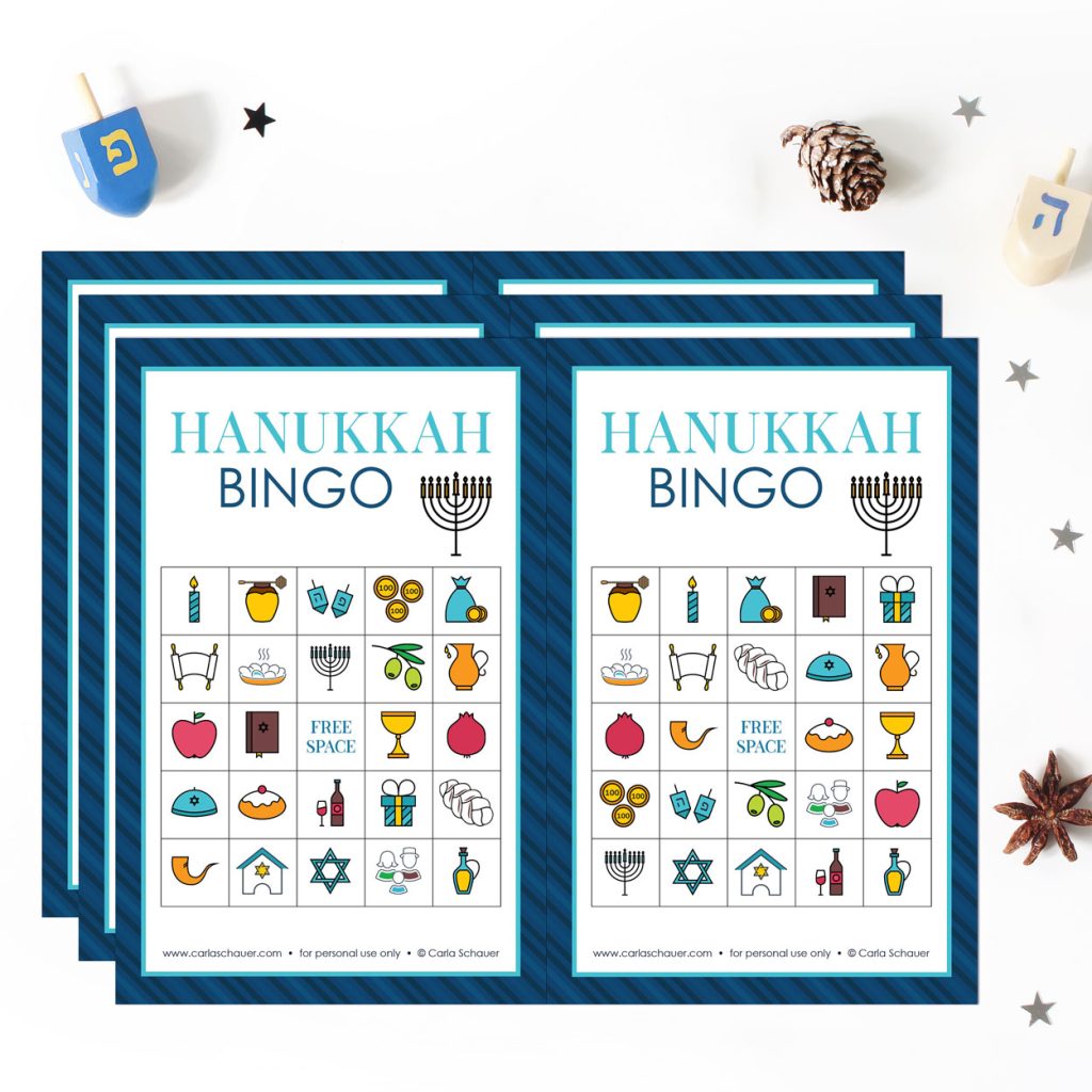 3 printed pages of Hanukkah bingo cards, each with 2 cards containing tradional Hanukkah symbols and a blue border. Pages are lying on a white background surrounded with dreidels, pinecones, and silver star confetti.