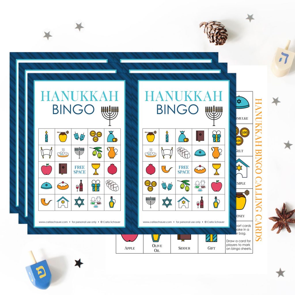 3 printed pages of Hanukkah bingo cards, each with 2 cards containing tradional Hanukkah symbols and a blue border, lying on top of a page printed with the same icons and labels. Pages are lying on a white background surrounded with dreidels, pinecones, and silver star confetti.