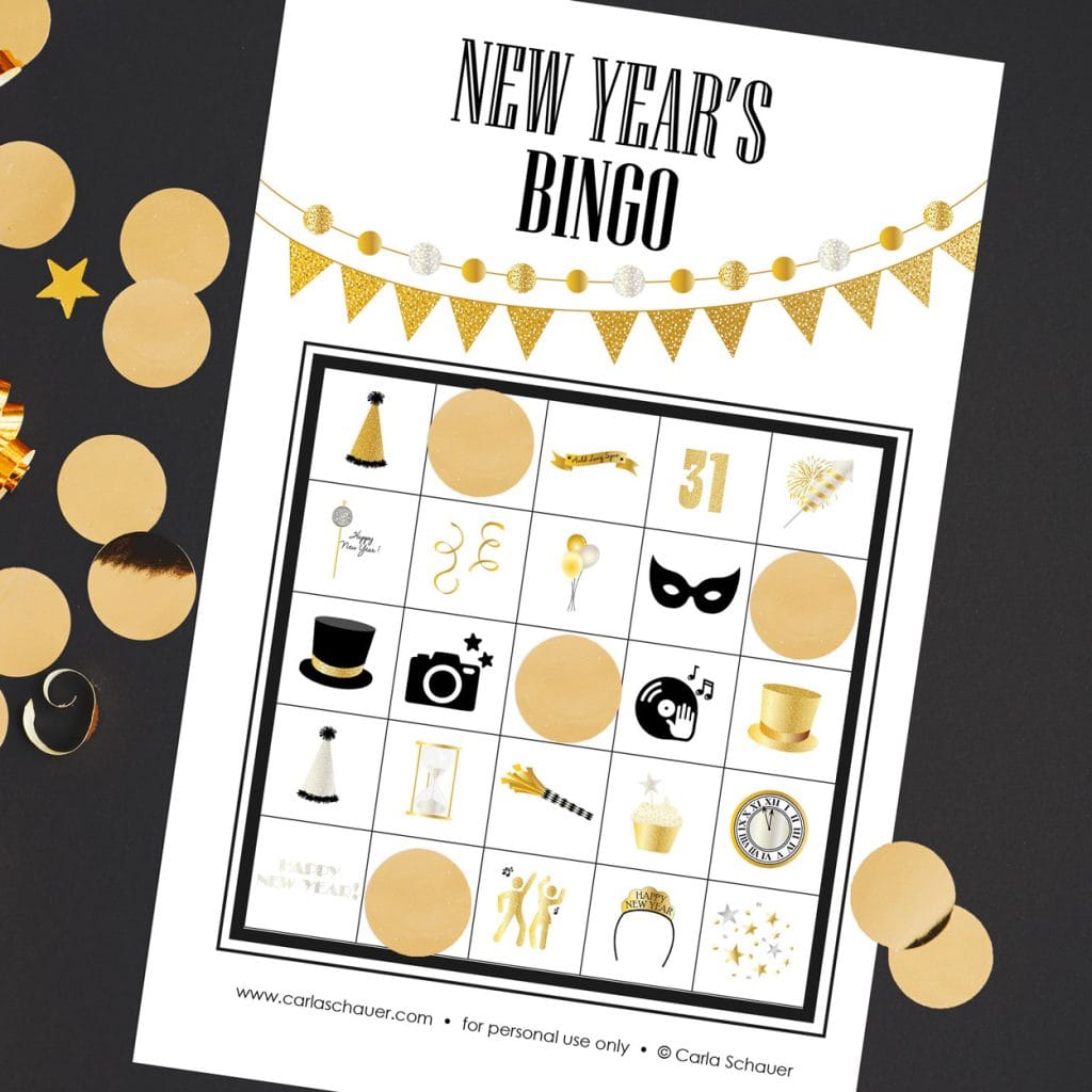 White New Year's Bingo card, lying angled on a black background with shiny gold circles. Each bingo sheet has a 5x5 grid of party icons, a gold pennant banner, and black text that reads "New Year's BINGO." Gold Circles mark of 4 spaces on the card.