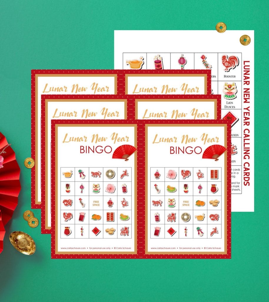 3 Printed Lunar New Year Bingo Cards, white with red border and grid with 25 holiday icons. Cards are lying on printed calling card page with same icons. Background is green, with gold trinkets and red fans.