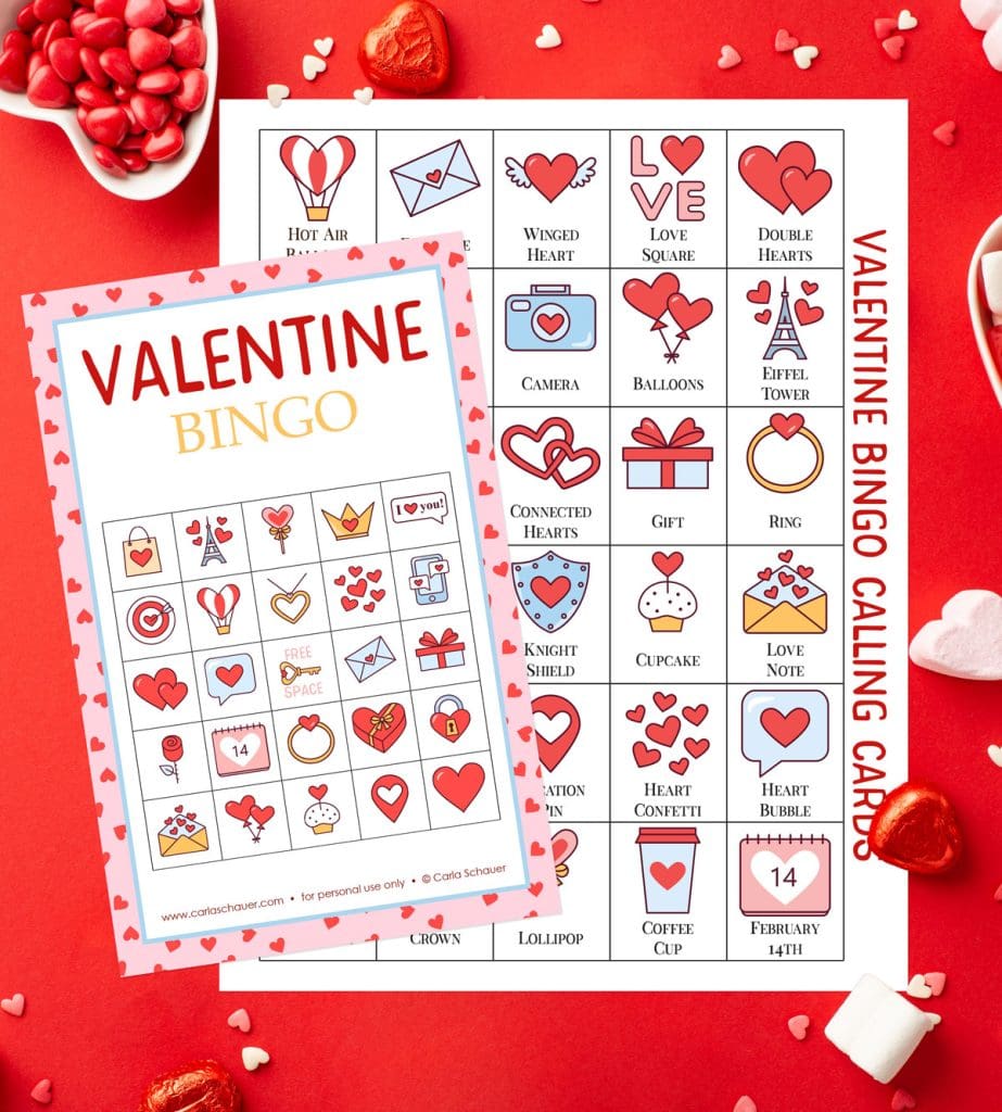 Printed Valentine Bingo card, white with a pink/red heart border and a 5x5 grid of valentine icons, along with a printed calling card sheet containing the same icons. Pages are lying on a red background with scattered Valentine candies.
